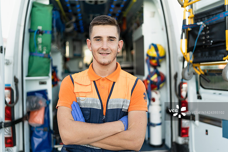 面带微笑的年轻急救人员在救护车旁手臂交叉的肖像图片素材