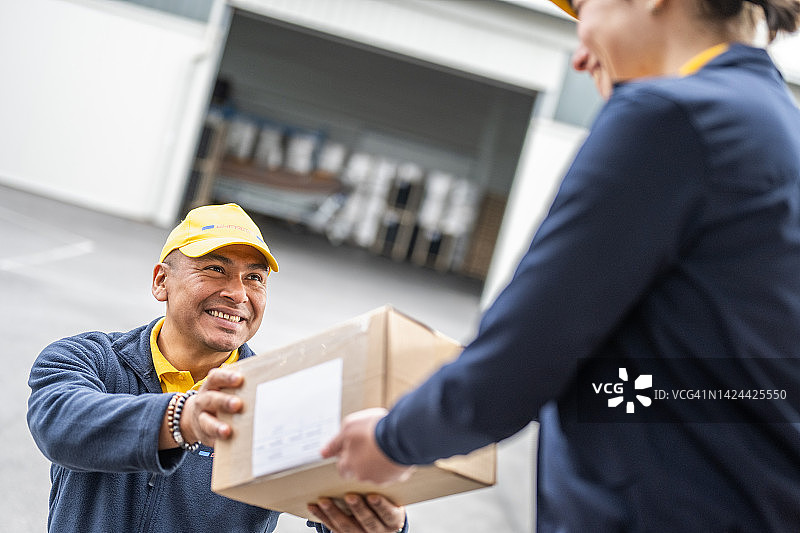 仓库工人微笑地将纸板箱交给快递员图片素材