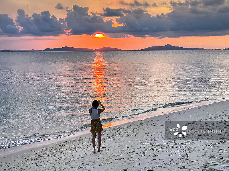 在热带岛屿上拍摄海滩日落的人图片素材