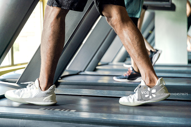 年轻健壮的男人在跑步机上跑步，腿部特写图片素材
