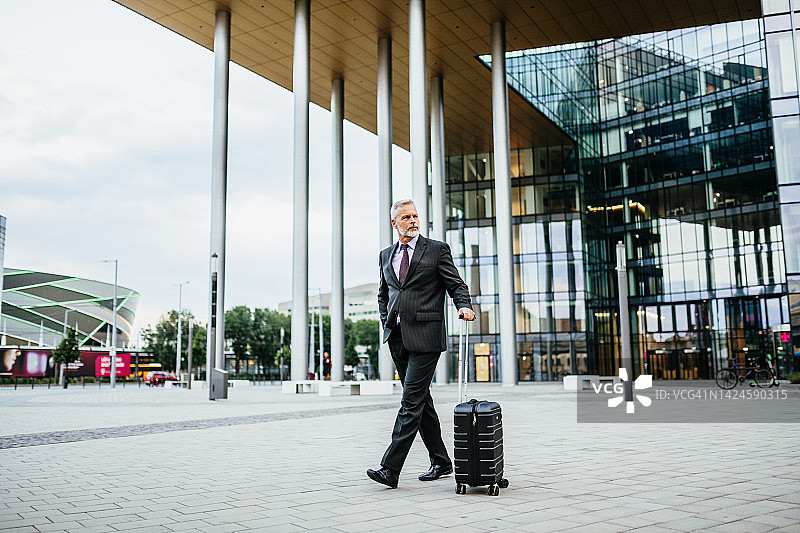 身穿全套西装的成熟商人在金融区拉着行李箱行走图片素材