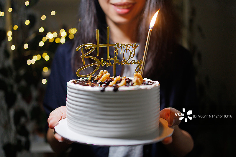 女人手持装饰着金色生日快乐标志和蜡烛的生日蛋糕图片素材