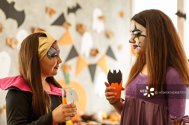 万圣节派对上穿着节日服装、化着彩妆，边喝饮料边聊天的女孩们图片素材