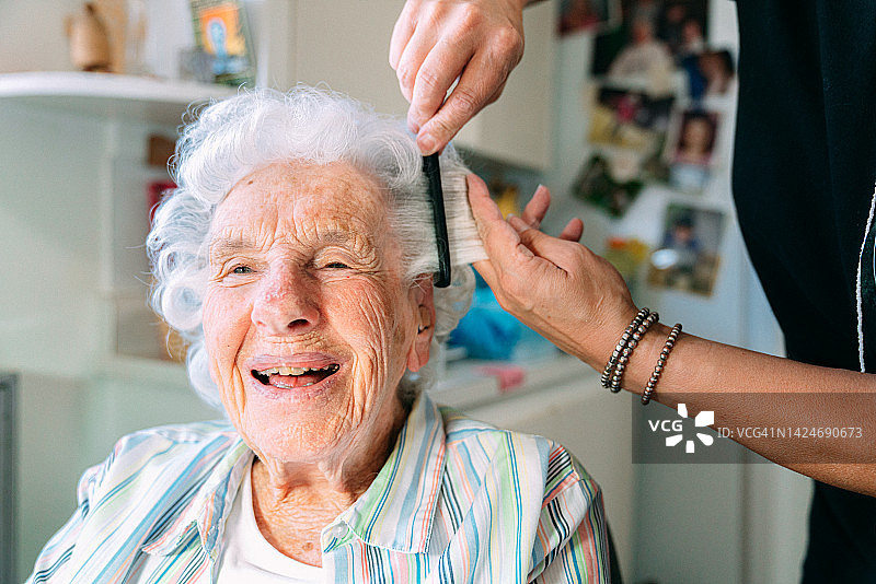 年长的白人妇女在家中由专业护理造型师梳头的广角照片图片素材