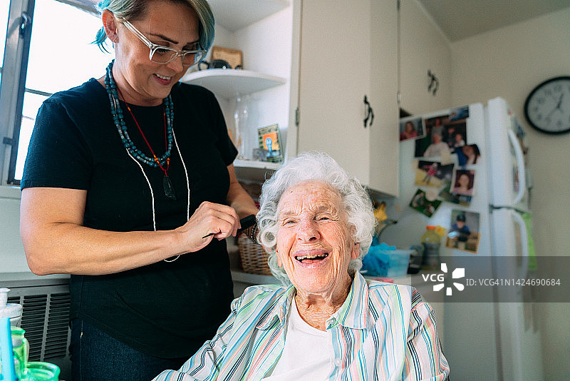 年长的白人妇女在家中由专业护理造型师梳头的广角照片图片素材