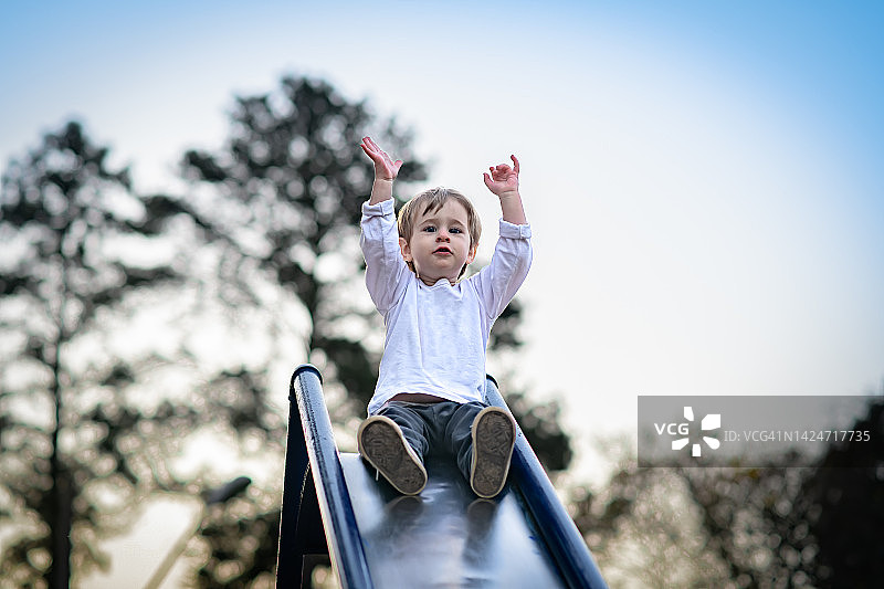 快乐的幼儿男孩准备在操场上滑滑梯图片素材