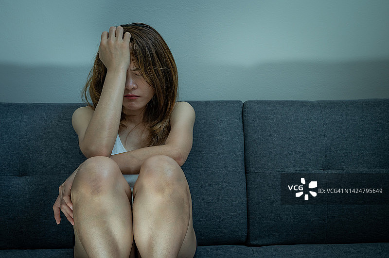 亚洲女性独自坐在沙发上感到压力。抑郁症是一种对自我、他人和生活的高度消极思维图片素材