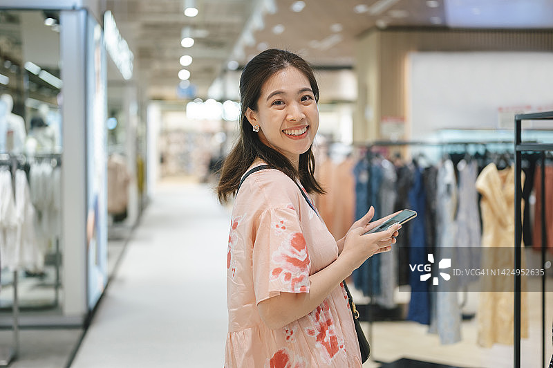 自信的亚洲女性在精品店购物浏览服装，进行手机比价图片素材