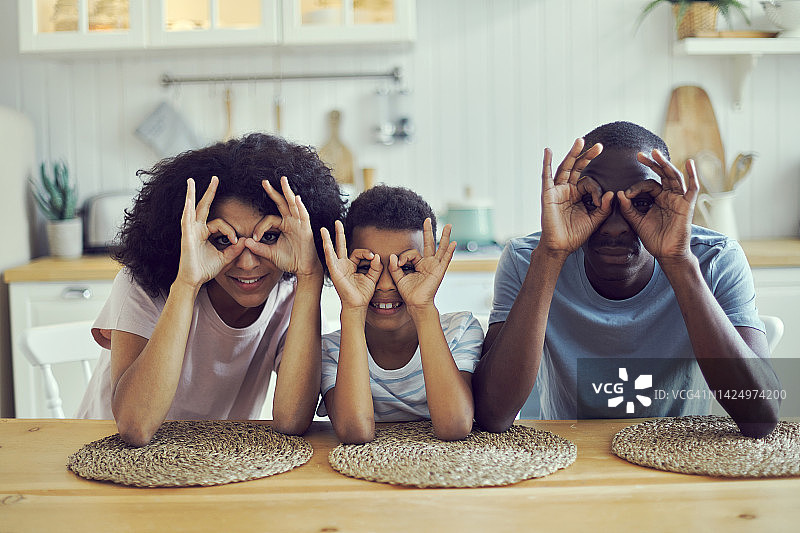 父母和儿子用手指比划眼镜形状，微笑看向镜头，宣传眼镜镜片图片素材