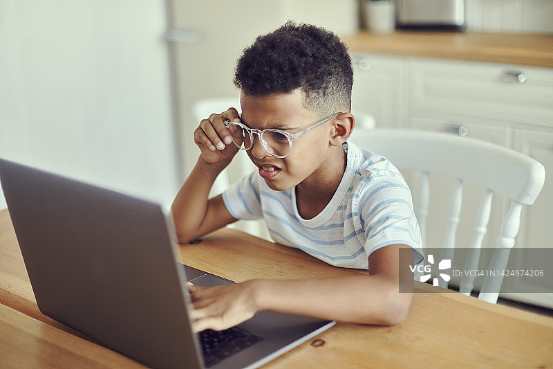 戴眼镜的非洲小男孩看笔记本电脑屏幕，因过度使用无线技术导致视力障碍图片素材