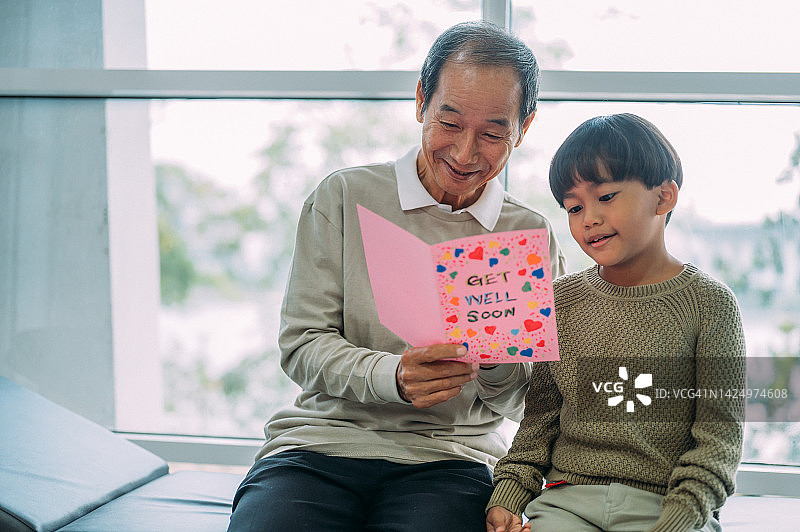 亚洲老年男子收到并阅读来自孙辈的慰问卡，他坐在医院病房里图片素材