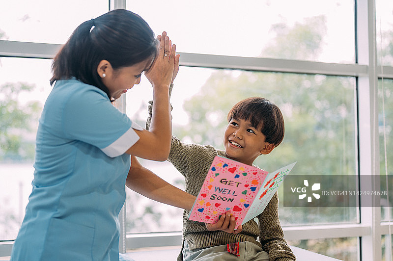 在医院病房里，亚裔儿童与护士击掌，收到慰问卡图片素材