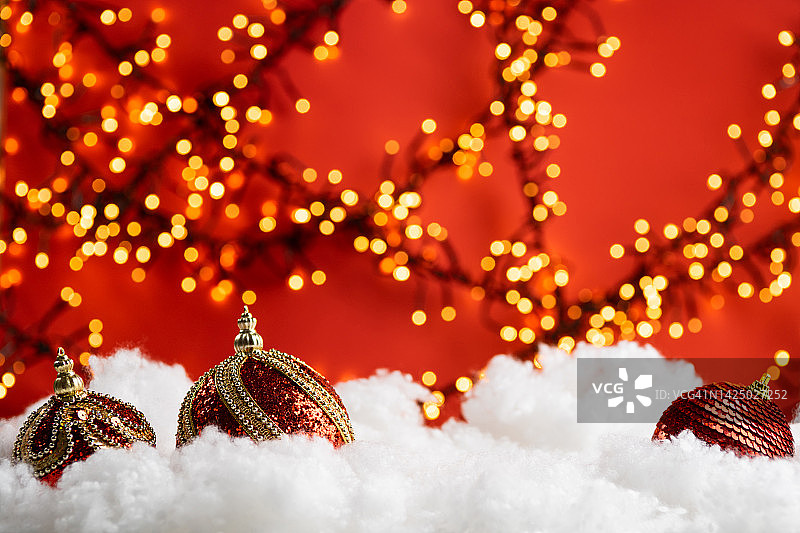红色背景金色灯光下的雪中圣诞球图片素材