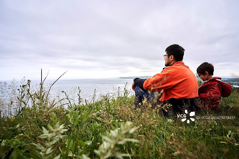 父子俩坐在山上俯瞰大海图片素材