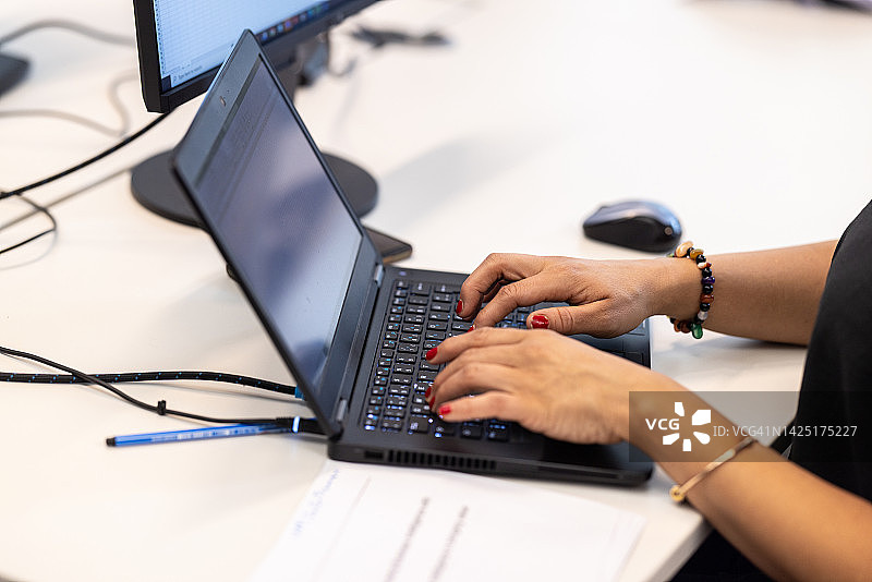 女子在办公室的桌子上用笔记本电脑键盘打字图片素材