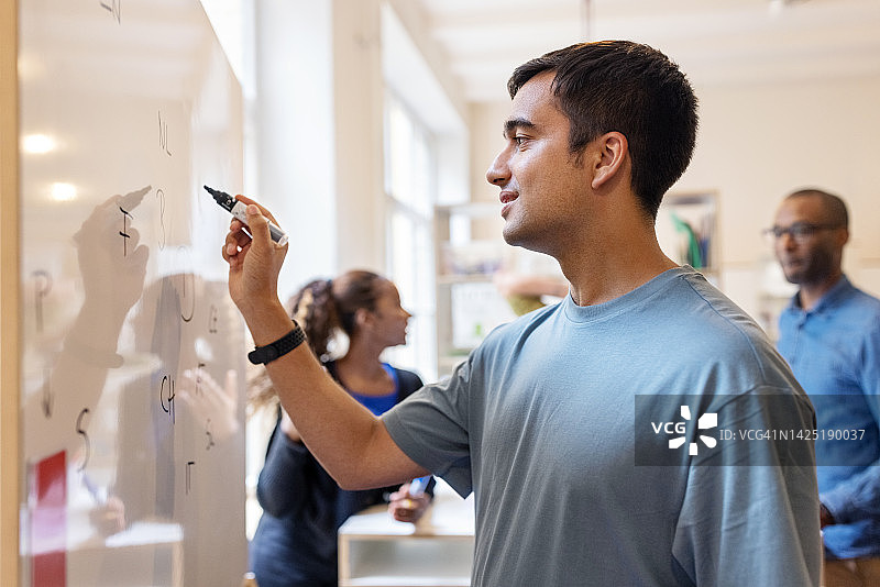 年轻的亚洲男人在白板上书写，同事在后台讨论图片素材