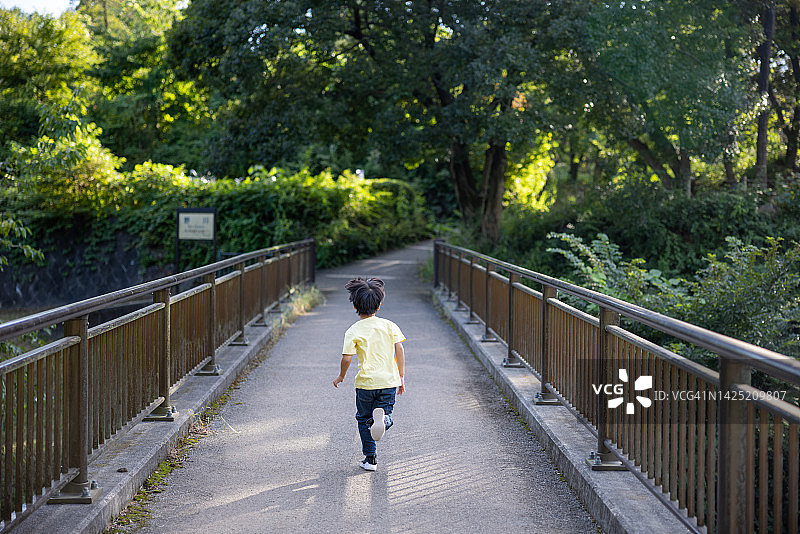 在公园桥上奔跑的男孩的后视图图片素材