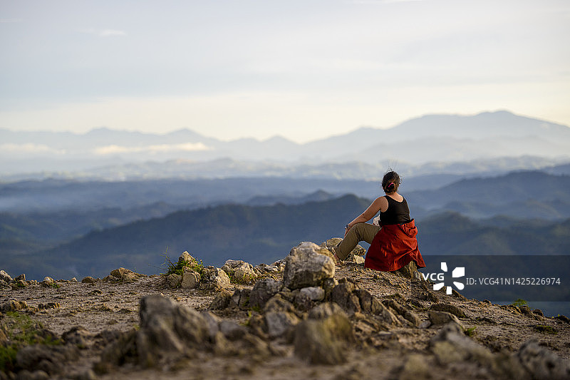 在日出时坐在岩石上的徒步旅行的年轻女人图片素材