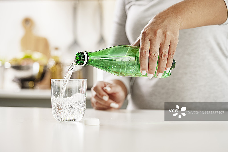 将矿泉水从绿色塑料瓶倒入玻璃杯中图片素材