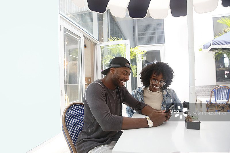 一位戴棒球帽的非裔美国男人在户外咖啡店与一位有卷发的非裔美国女人交谈图片素材