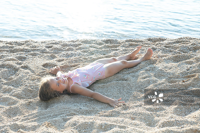 小女孩躺在海边的沙滩上。图片素材