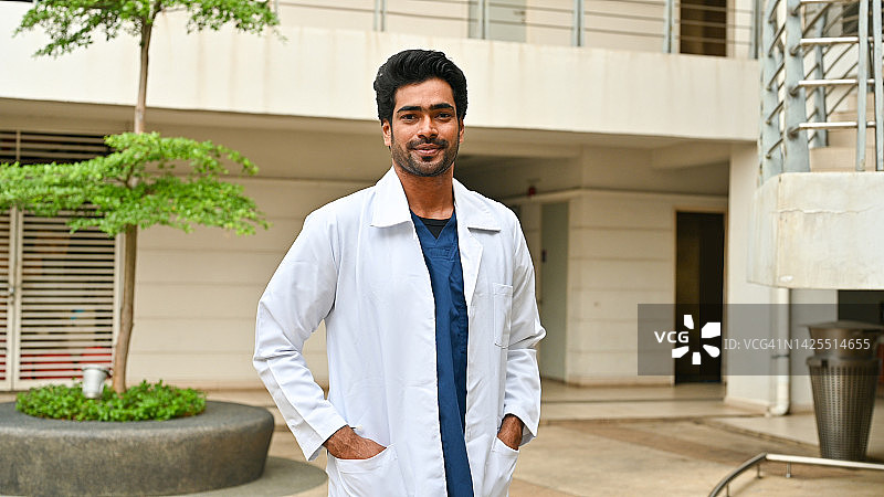 男性医疗保健专业人员：一位印度裔男医生在医院走廊里微笑图片素材