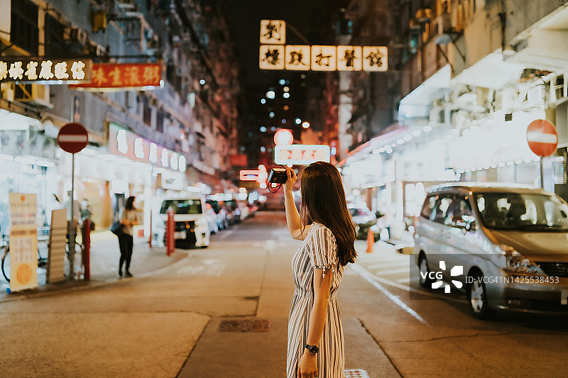 年轻亚洲女人在香港街头拍摄城市夜景，背景是中国商店招牌图片素材