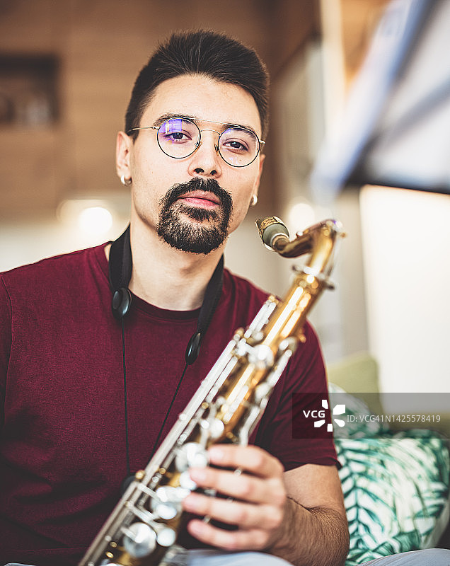 在家练习萨克斯管的年轻男音乐家肖像图片素材