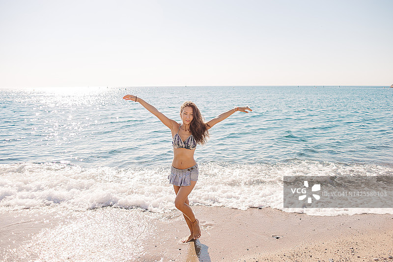 在阳光明媚的沙滩上摆姿势的泳装年轻女人图片素材