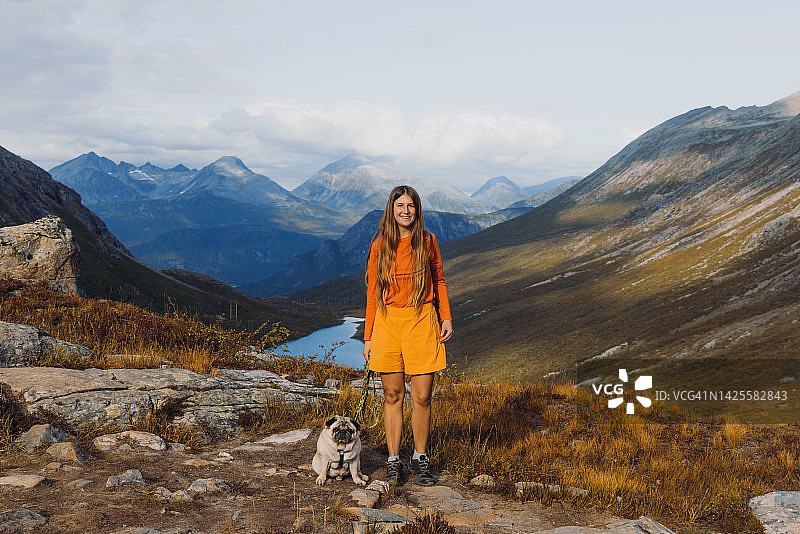 在挪威秋季，徒步旅行的女人和狗在欣赏风景秀丽的山景图片素材