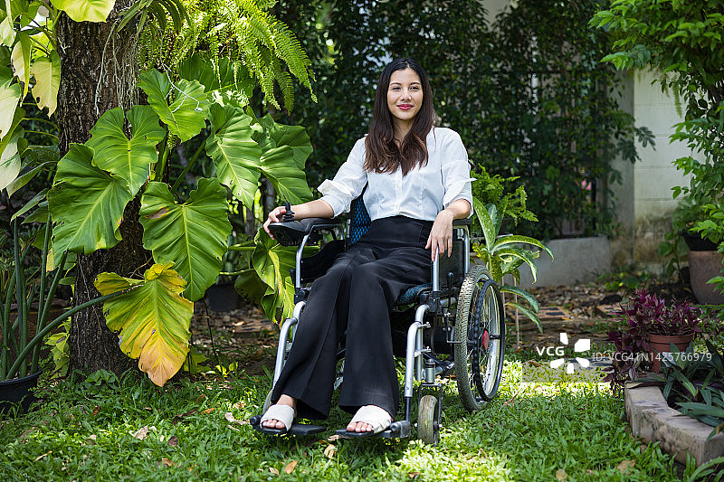 在花园里使用电动轮椅的快乐亚洲女性图片素材