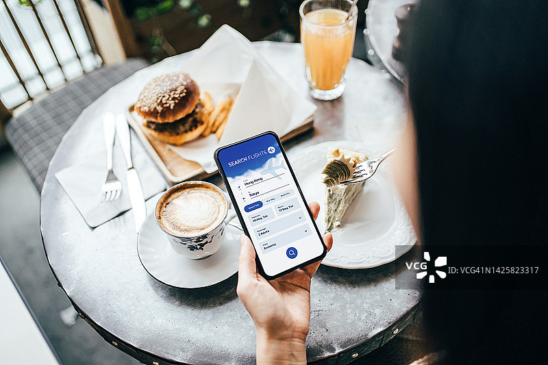 年轻女性在咖啡馆用智能手机在线预订机票的肩上视角。旅行规划。在线预订假期。旅行和度假概念。商务人士计划出差图片素材