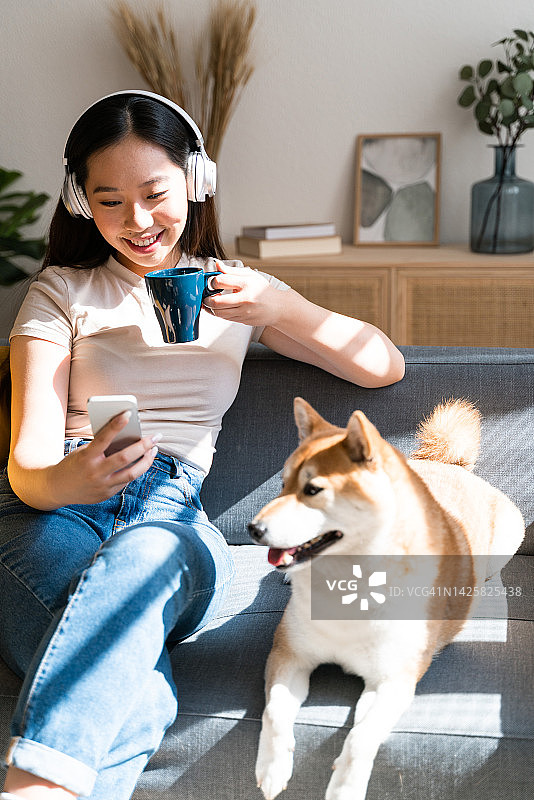 美丽的女人在家用手机进行视频通话，坐在她的狗旁边图片素材