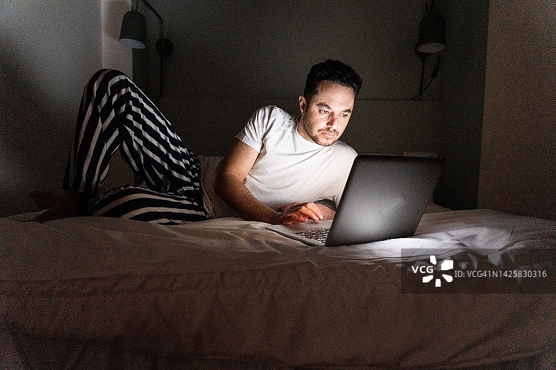 男人晚上在床上用笔记本电脑微笑图片素材