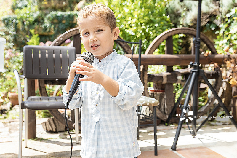 阳光明媚的日子里，快乐的小男孩在户外用麦克风唱歌图片素材