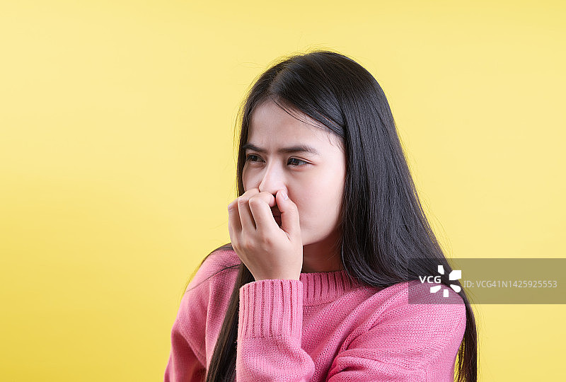 聪明的年轻女子捂着鼻子，因为黄色背景上有异味图片素材