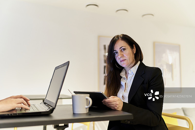 身穿黑色正装、留着棕色长发，在办公室使用平板电脑工作的女高管图片素材