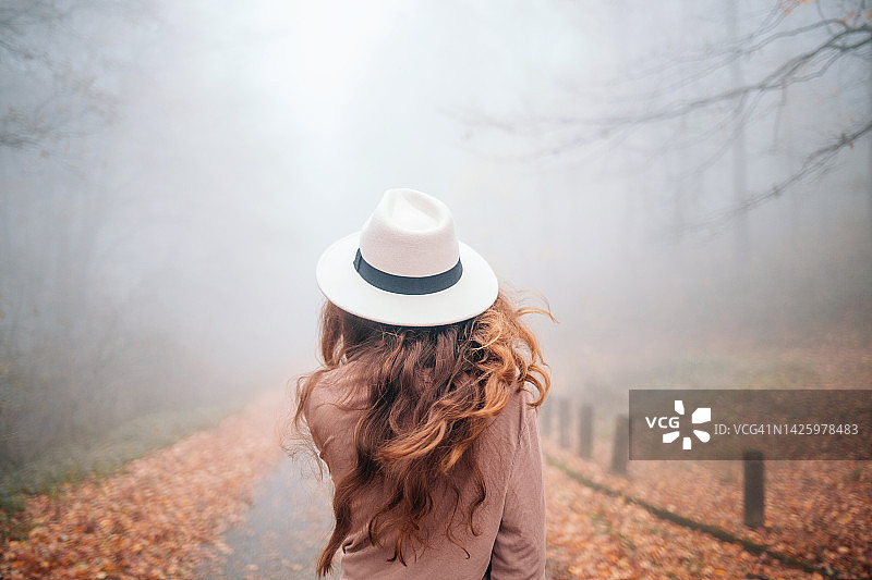 女人在雾蒙蒙的秋季森林的道路上行走图片素材