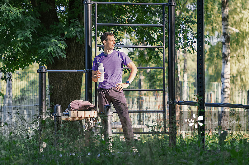 户外运动后休息的健壮男人，在公园里使用单杠图片素材