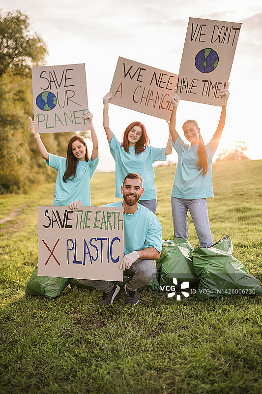 一群快乐的志愿者在清理完自然区域的垃圾后，举着写有铭文的纸板图片素材