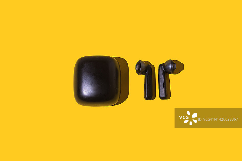 黄色背景上的无线黑色耳机和充电器：音频、音乐、广播、播客、无线和蓝牙技术概念图片素材