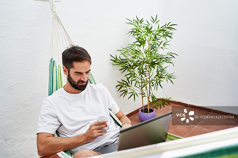 男人躺在吊床上使用笔记本电脑图片素材