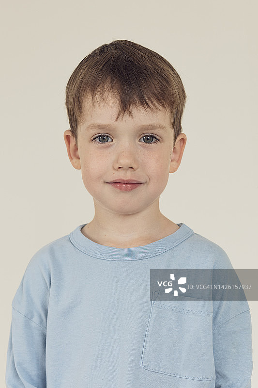 米色背景下，身穿蓝色长袖的5岁男孩的特写图片素材