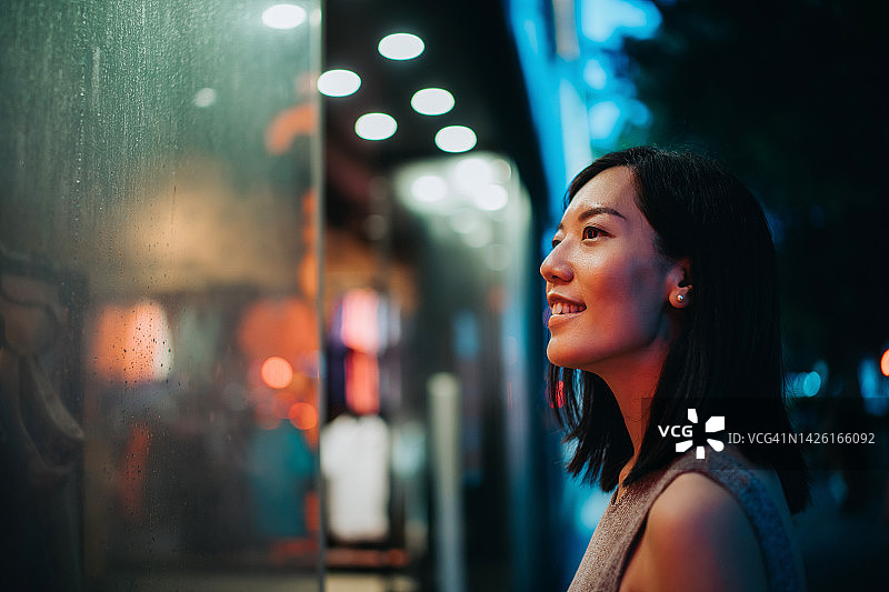 站在精品店前，看着橱窗的亚洲年轻女性，在城市里购物图片素材