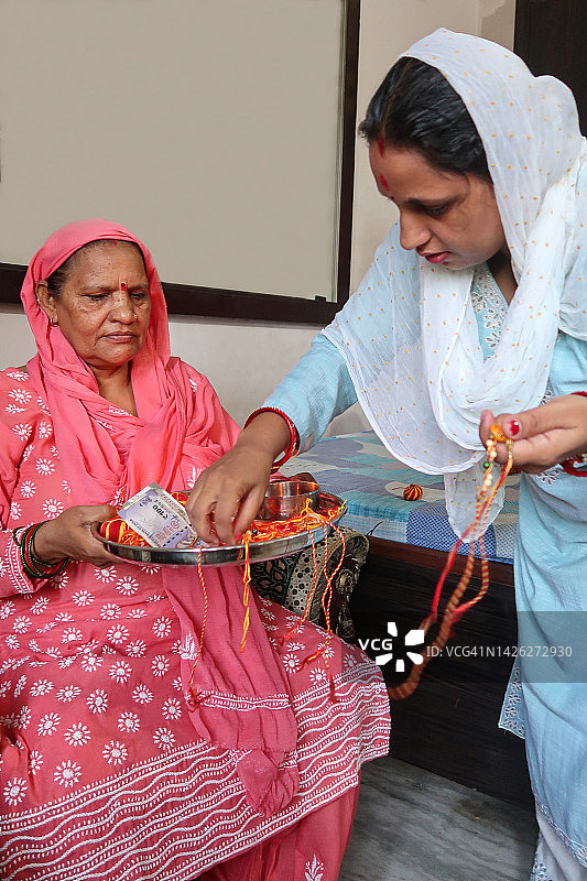 印度母亲拿着涂有红色粉末的Rakhi盘子，女儿挑选手镯图片素材
