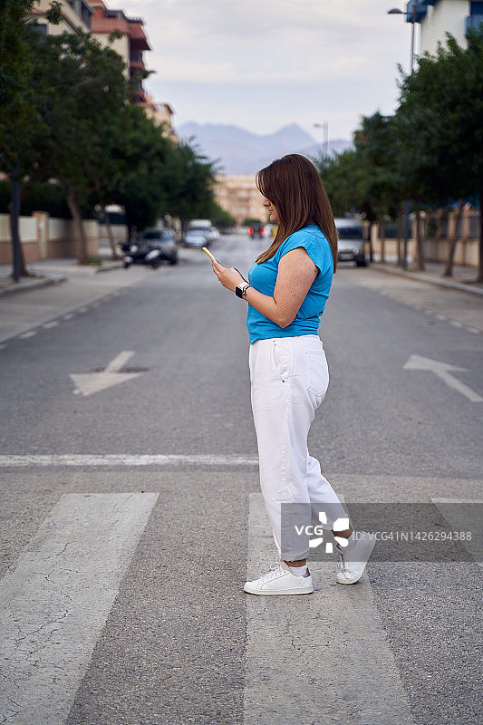 年轻女子在人行横道过马路，低头看手机的侧面照图片素材