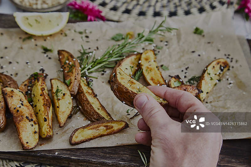 男人拿着加纯素调味料的健康烤土豆，在木制砧板上图片素材