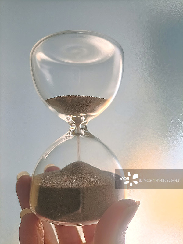 女性手持沙漏，棕色细沙流逝图片素材