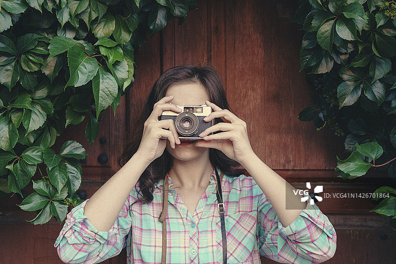 年轻女子手持模拟相机并通过取景器观看图片素材
