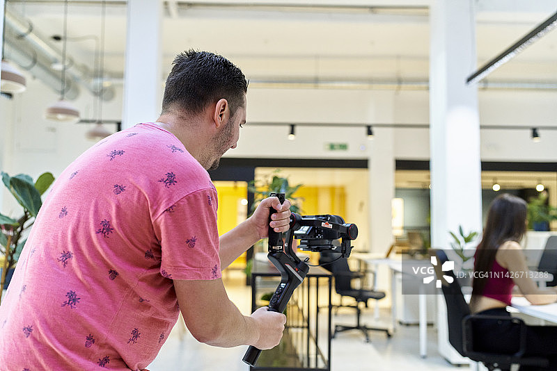 专业摄影师正在一个现代化的办公室里拍摄照片。美丽的年轻女子坐在桌子前摆姿势拍照。图片素材